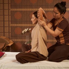 Relaxed female patient sitting on couch during shoulder stretch performed by masseuse